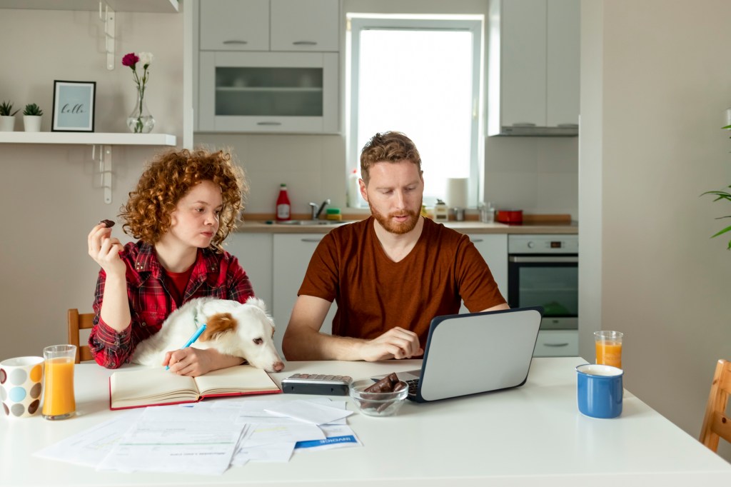 Couple does taxes at kitchen table with dog.